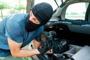 a man with gloves and a mask steals photography equipment from a car - insurance and legal issues
